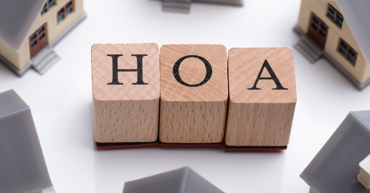 Tiny, grey and beige house models placed in a circle surrounding wooden letter blocks that spell out HOA.