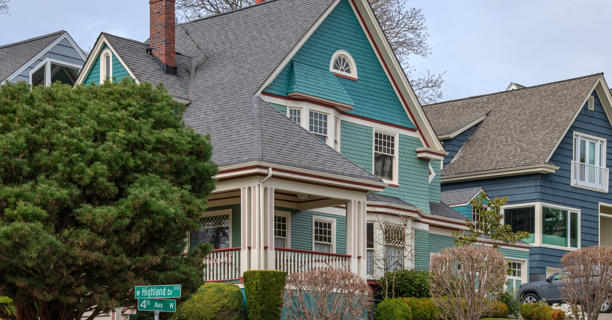 A row of similar, grey and blue houses lined up on the side of the neighborhood street with lush, well-kept landscaping in the front.