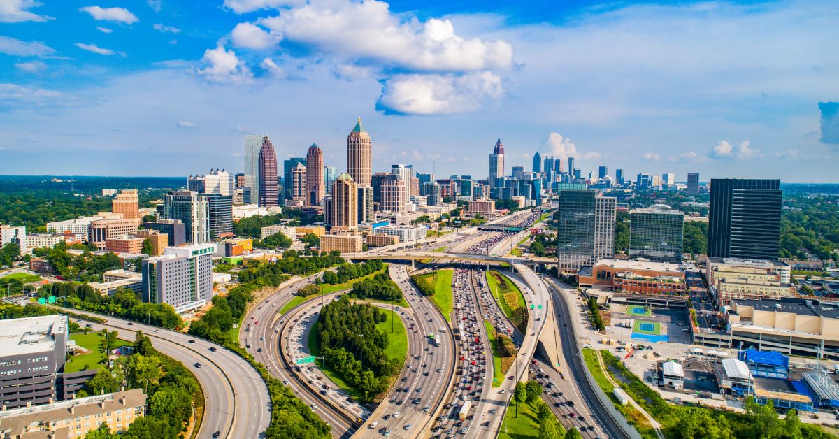 An aerial view of Atlanta, Georgia, with skyscrapers and highways weaving through the city under a bright blue sky.