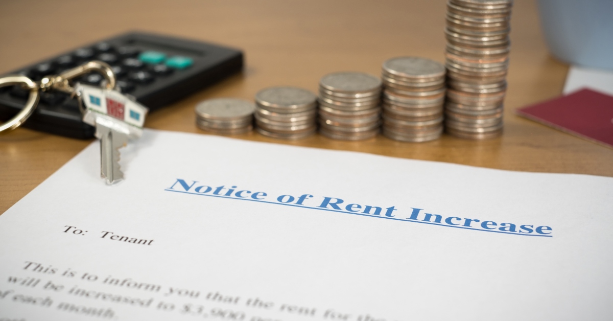 A close-up of the top of a rent increase notice document with a set of keys and coins on top and a calculator in the background.