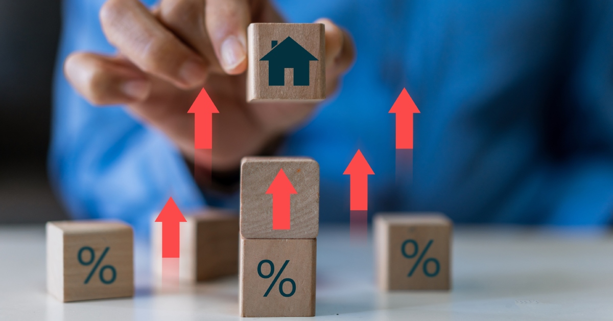 A man in a blue dress shirt places down a wooden block with a house symbol on it onto other blocks. There are upward red arrows.