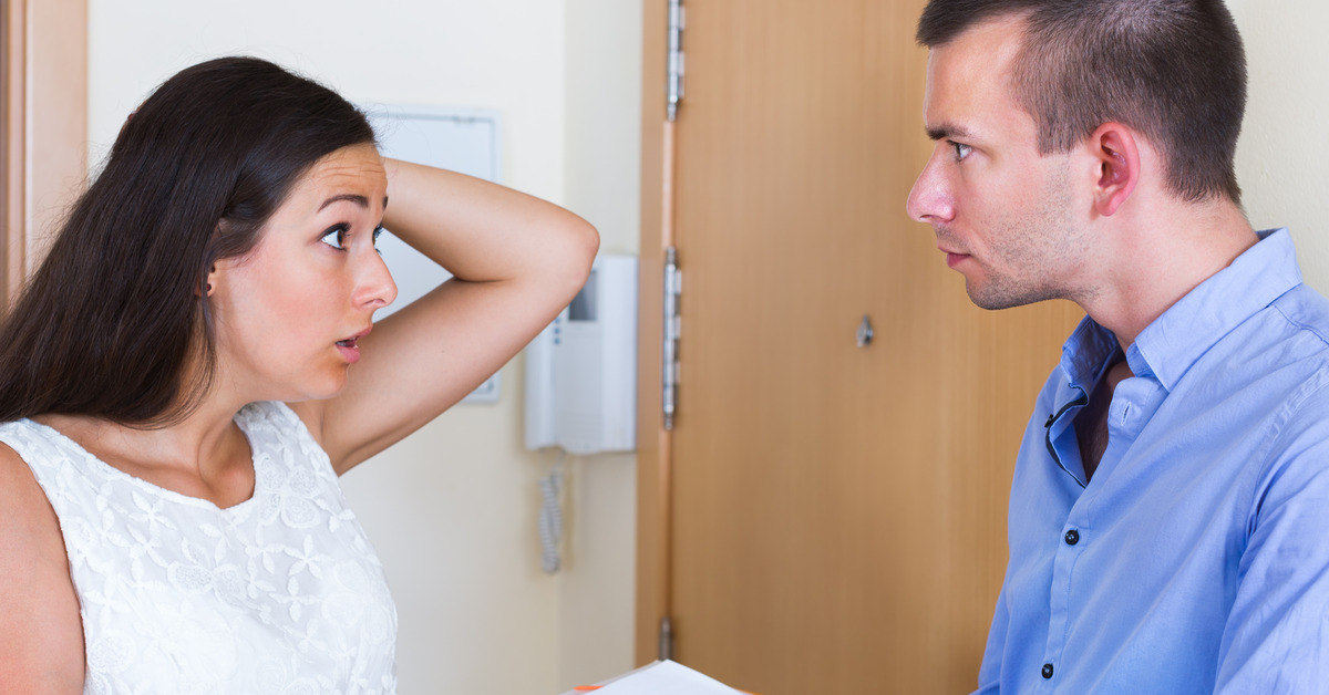 A male landlord pointing to a paper on a folder confronts a confused female tenant with her hand on her head.