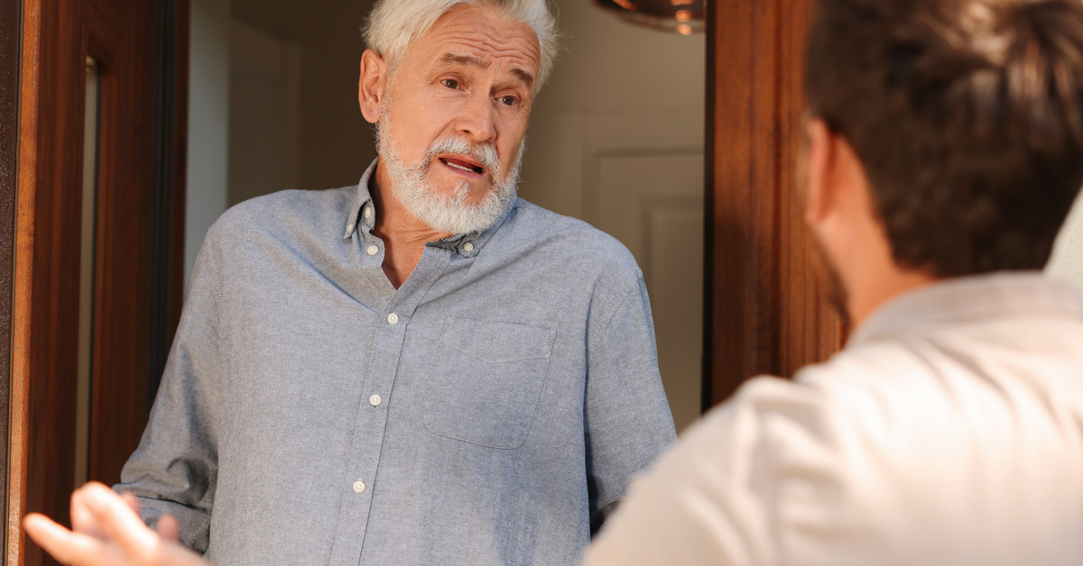 An older man steps outside his house to a man raising his hands who is arguing with the older man at his front door.