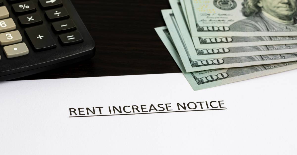 A document reading "rent increase notice" with a letter addressed to a tenant sits next to a calculator and hundred dollar bills.